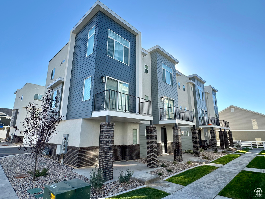 View of property featuring stucco siding, a balcony, a residential view, and brick siding