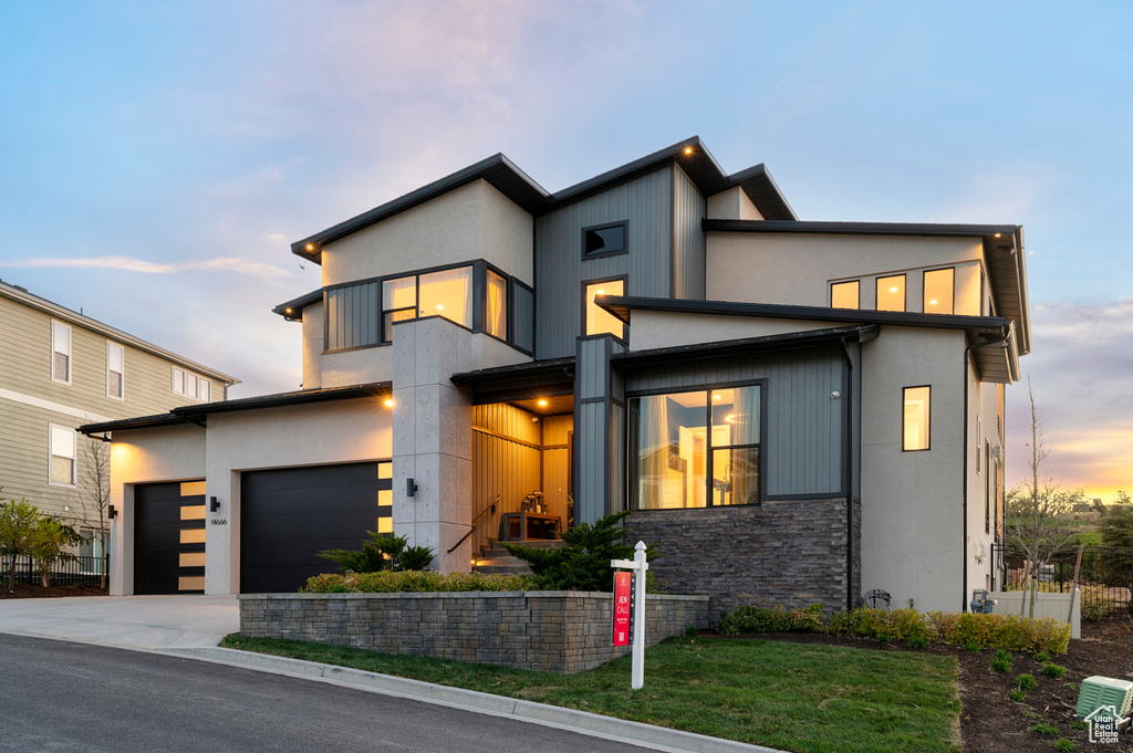 Contemporary home featuring stone siding, driveway, an attached garage, a yard, and stucco siding