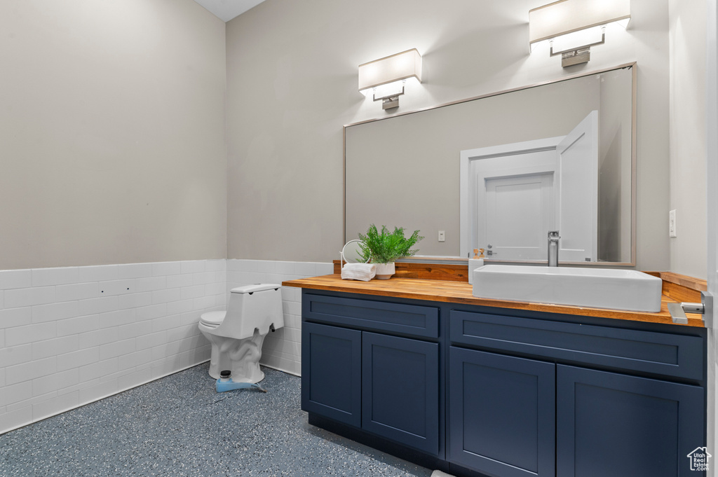 Bathroom featuring wainscoting, toilet, vanity, and tile walls