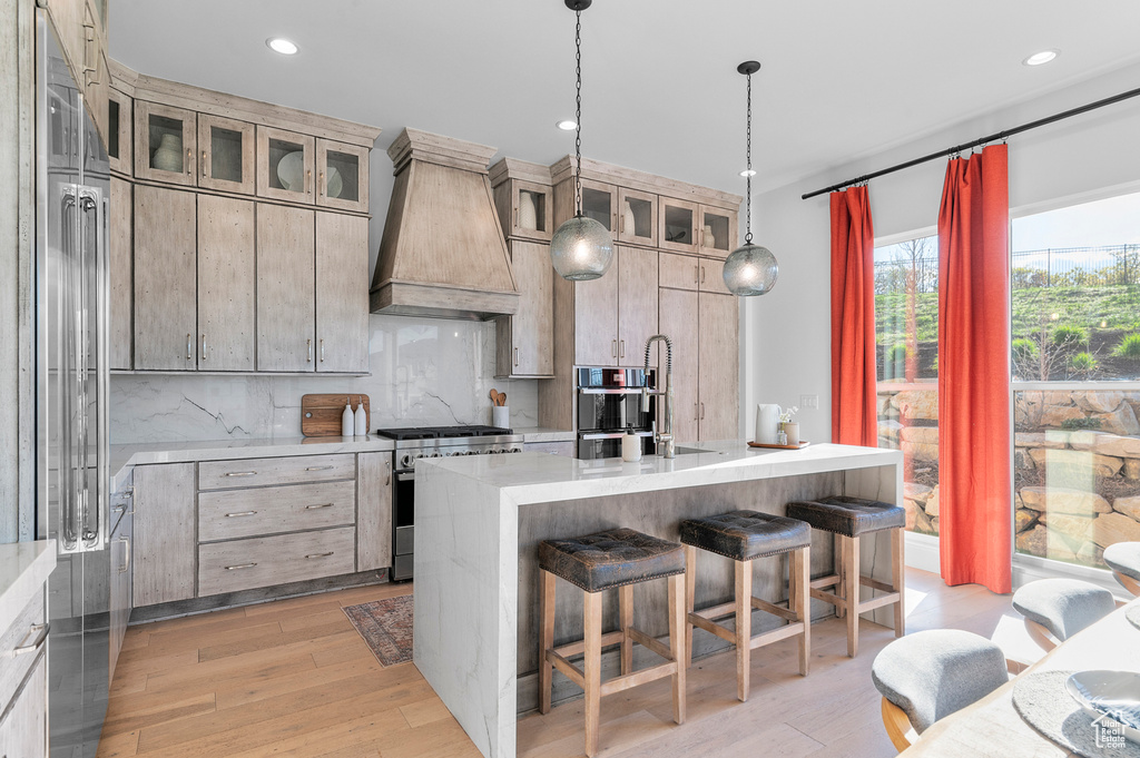 Kitchen with premium range hood, gas stove, a kitchen breakfast bar, light countertops, and a kitchen island with sink