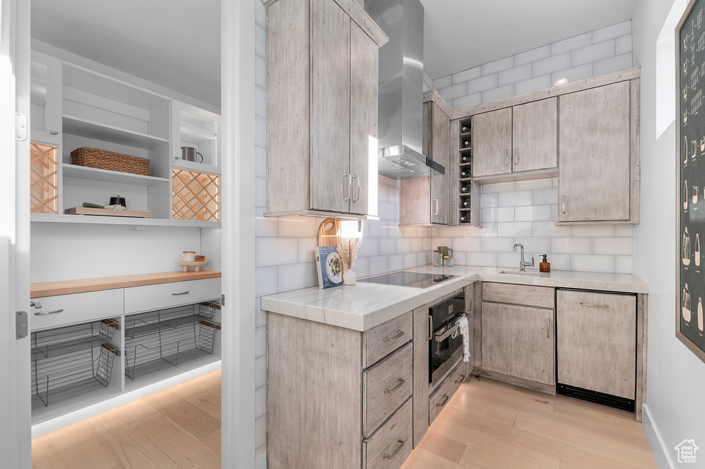 Kitchen with oven, light wood-type flooring, wall chimney range hood, light countertops, and open shelves