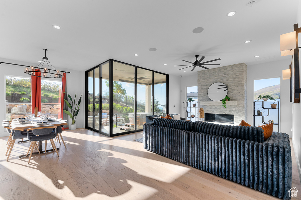 Living room featuring light wood-style flooring, a chandelier, a stone fireplace, recessed lighting, and ceiling fan
