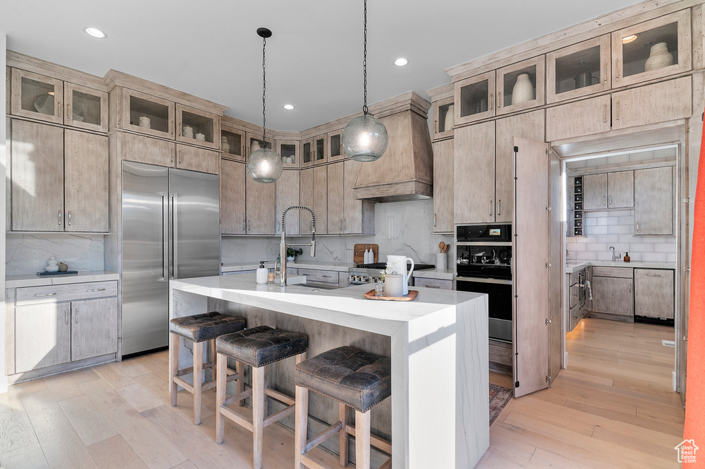 Kitchen with stainless steel built in refrigerator, backsplash, light countertops, light wood-type flooring, and recessed lighting