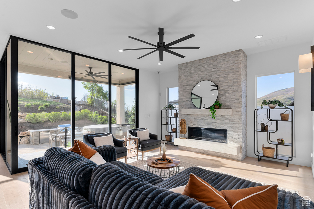 Living room featuring a ceiling fan, healthy amount of natural light, wood finished floors, a stone fireplace, and recessed lighting