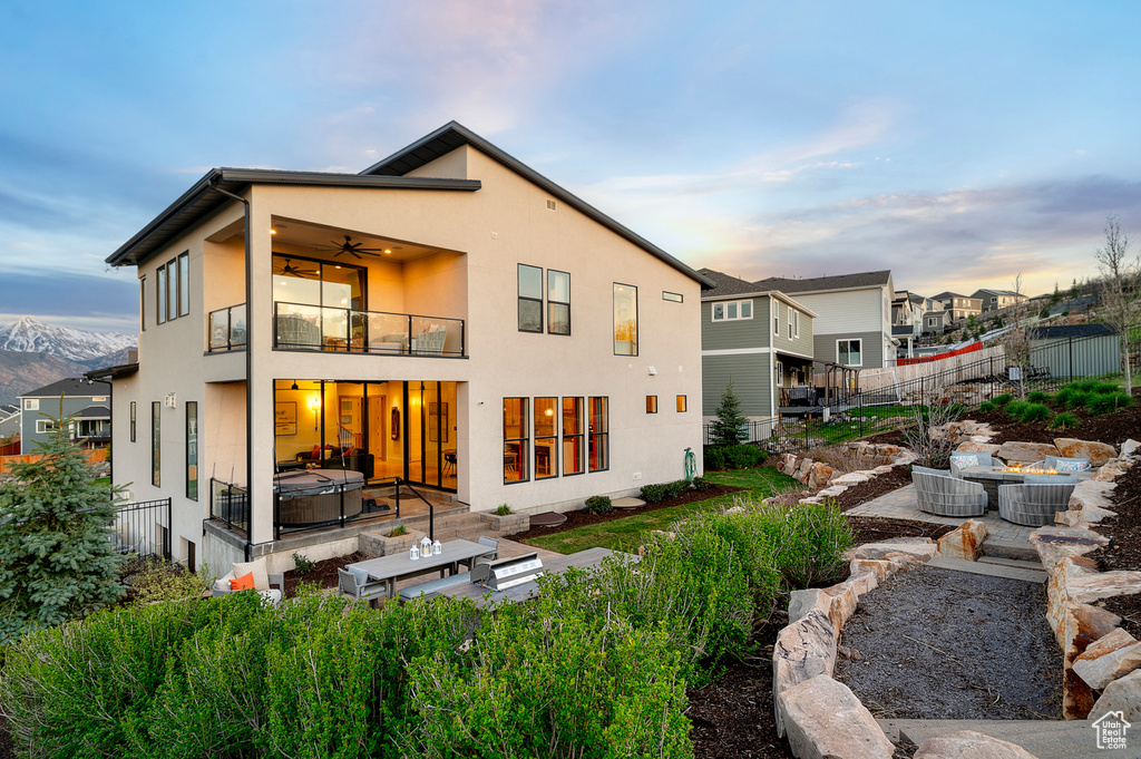 Back of house at dusk with a balcony, a hot tub, a ceiling fan, stucco siding, and a patio area