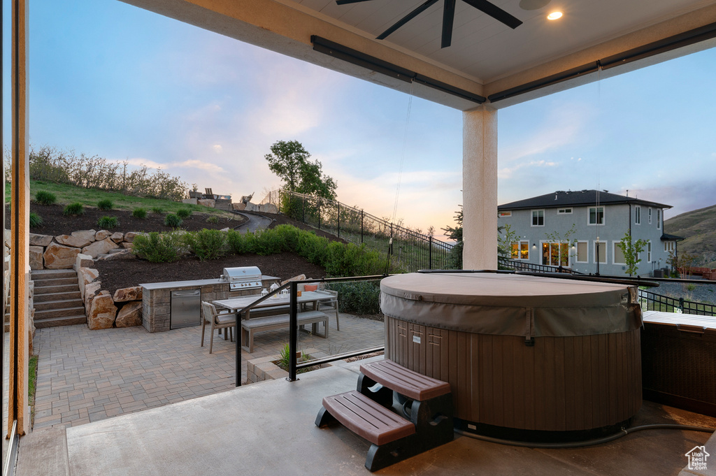 Patio terrace at dusk with a hot tub, exterior kitchen, and a ceiling fan