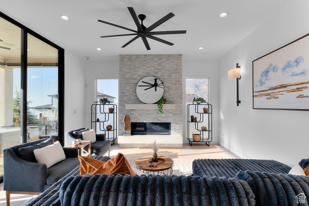 Living room with a ceiling fan, a stone fireplace, recessed lighting, and wood finished floors