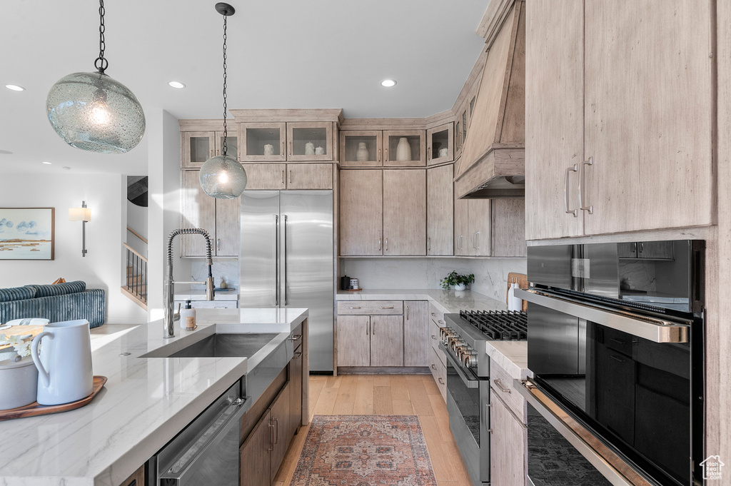 Kitchen featuring premium appliances, premium range hood, a sink, light wood-style floors, and recessed lighting