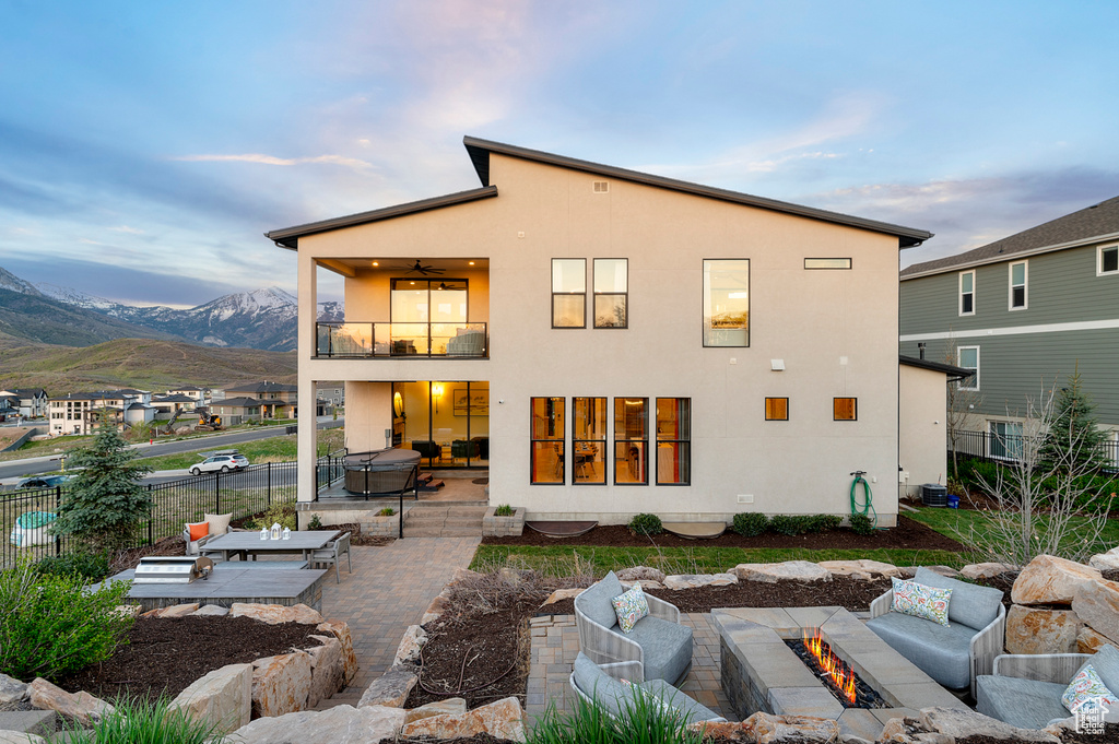 Back of house with a balcony, a patio area, an outdoor living space with a fire pit, and stucco siding