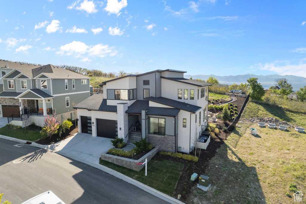 Contemporary house with concrete driveway, stucco siding, an attached garage, a mountain view, and a residential view