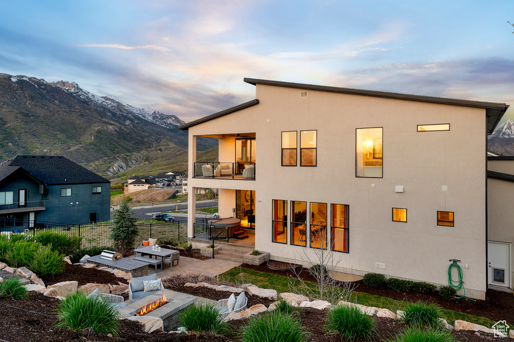 Back of property at dusk featuring a balcony, a patio area, fence, a mountain view, and stucco siding