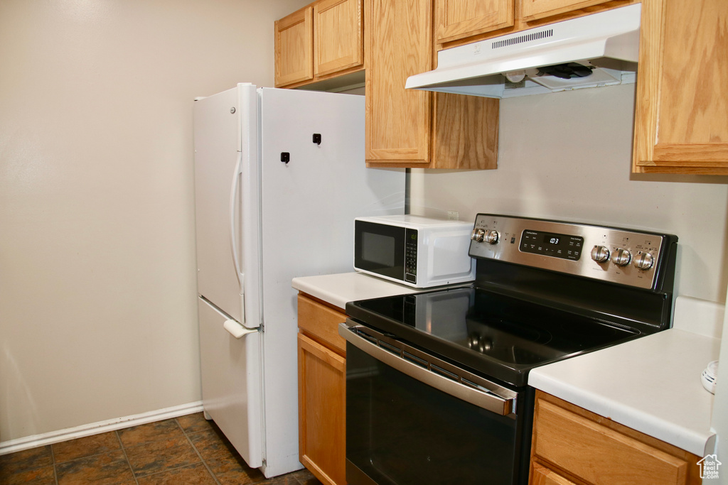 Kitchen with electric stove, under cabinet range hood, white microwave, baseboards, and light countertops