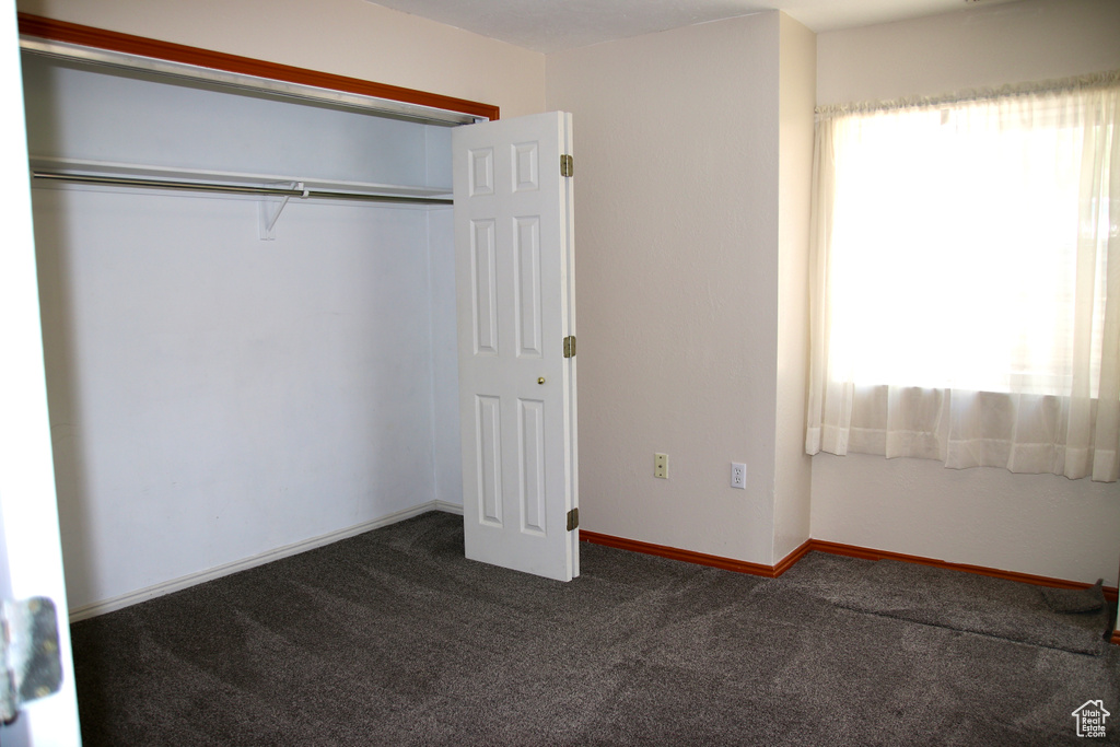 Unfurnished bedroom featuring dark colored carpet, a closet, and baseboards