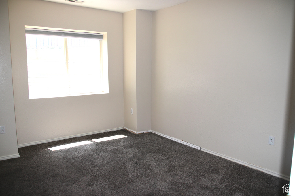 Empty room with plenty of natural light, dark carpet, and baseboards