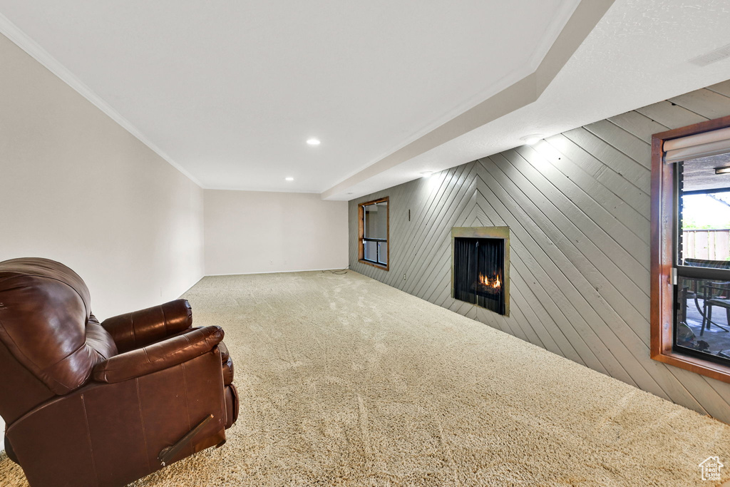 Living area featuring a warm lit fireplace, carpet, wooden walls, crown molding, and recessed lighting