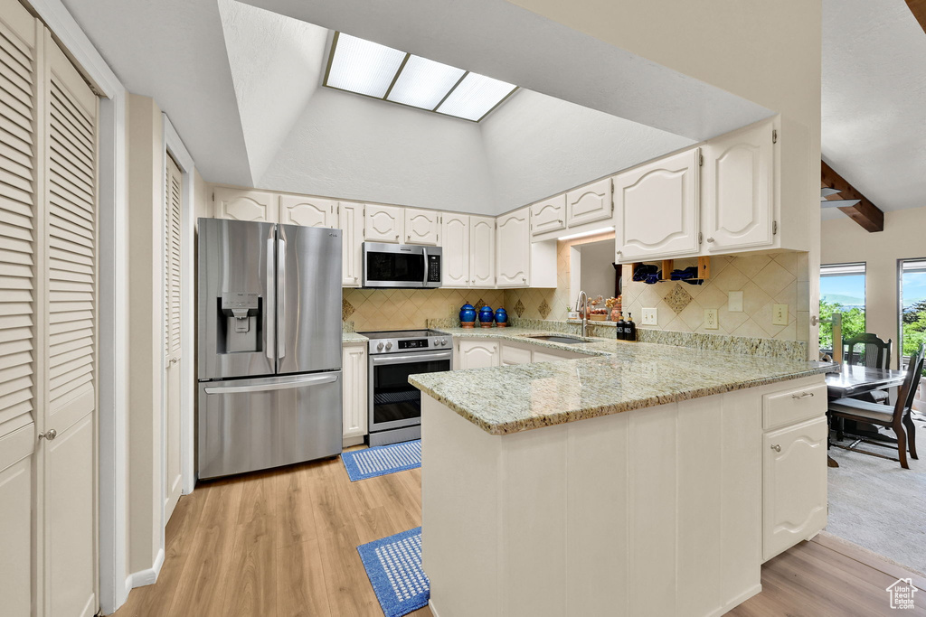 Kitchen featuring appliances with stainless steel finishes, a sink, a peninsula, light wood-type flooring, and backsplash