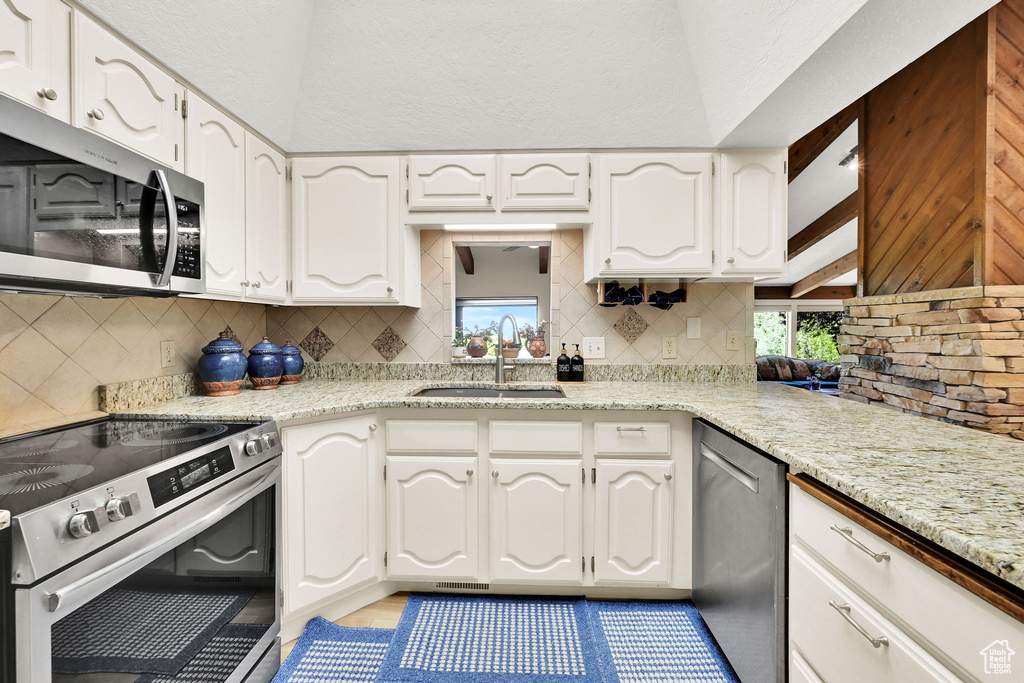 Kitchen featuring appliances with stainless steel finishes, a sink, backsplash, and white cabinets