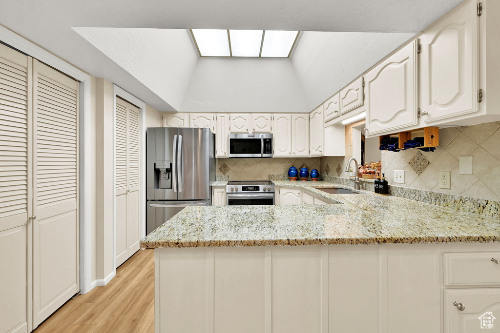 Kitchen featuring stainless steel appliances, a peninsula, a sink, backsplash, and light stone countertops