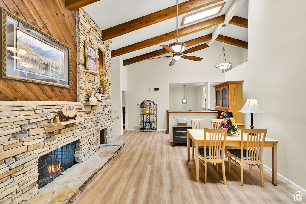 Dining area featuring high vaulted ceiling, light wood finished floors, a skylight, a fireplace, and baseboards
