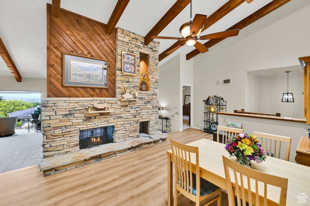 Dining room featuring high vaulted ceiling, a fireplace, beamed ceiling, ceiling fan, and wood finished floors