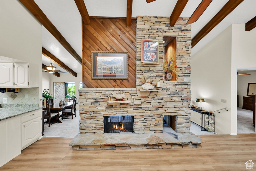 Living room with beam ceiling, high vaulted ceiling, a ceiling fan, a fireplace, and light wood-style floors