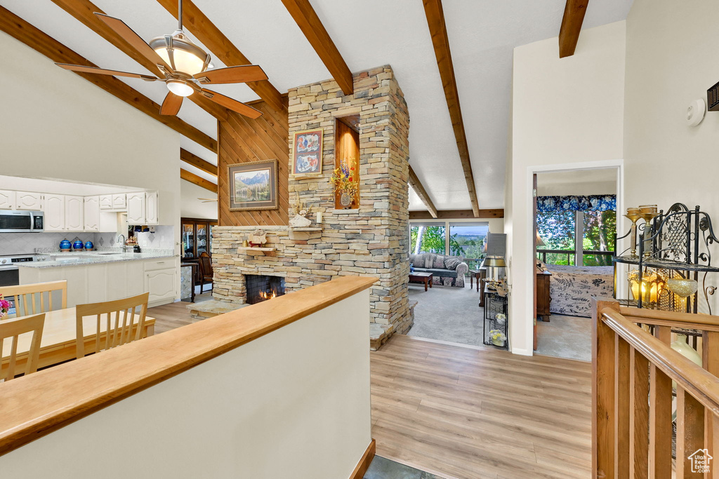 Living room with high vaulted ceiling, a stone fireplace, beamed ceiling, a ceiling fan, and light wood-type flooring