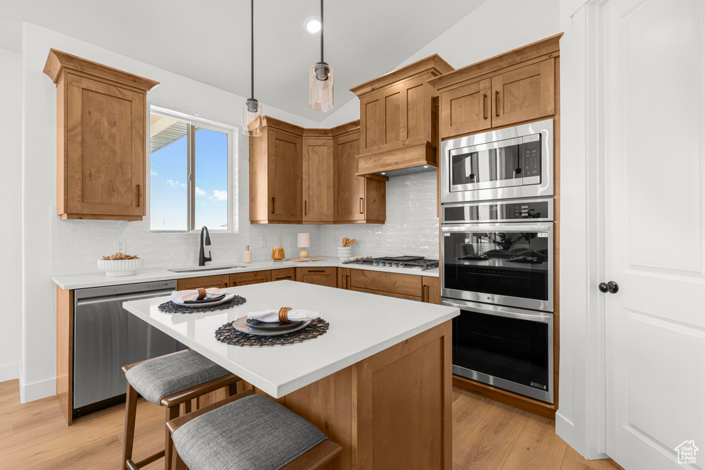Kitchen with appliances with stainless steel finishes, a sink, tasteful backsplash, light countertops, and light wood-style flooring