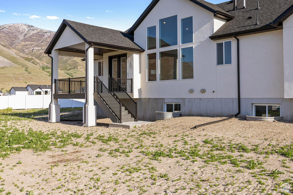 View of side of property featuring stairs, roof with shingles, a mountain view, stucco siding, and fence