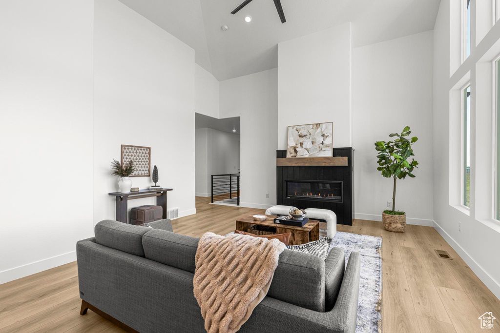 Living room featuring high vaulted ceiling, a ceiling fan, a glass covered fireplace, baseboards, and light wood-type flooring