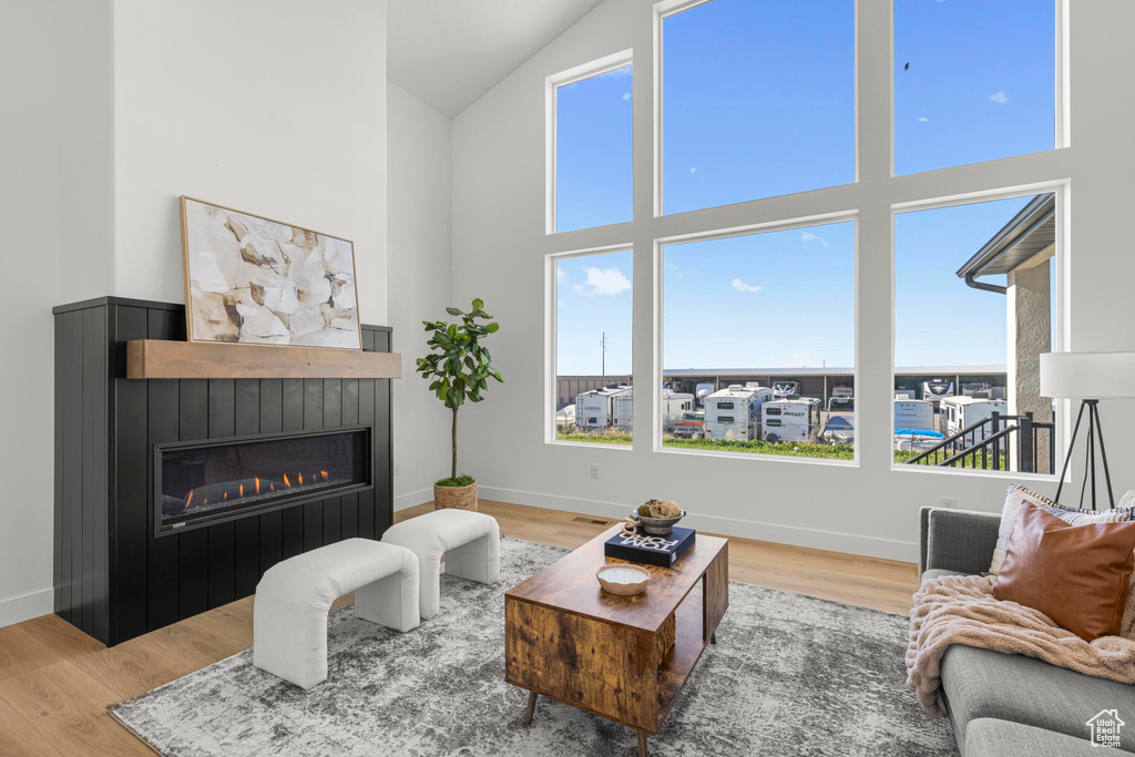 Living area featuring a glass covered fireplace, wood finished floors, high vaulted ceiling, and baseboards