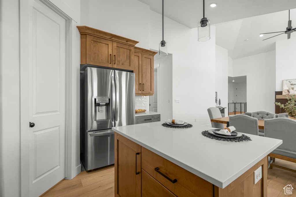 Kitchen with stainless steel refrigerator with ice dispenser, light wood-type flooring, light countertops, a center island, and open floor plan