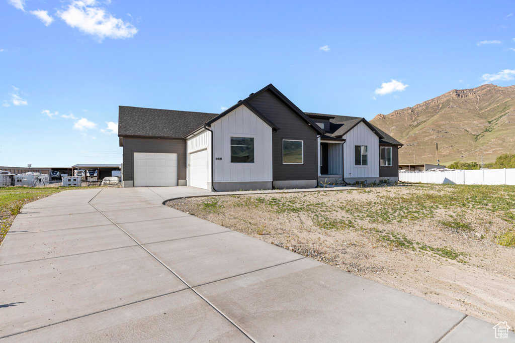 Modern farmhouse style home featuring an attached garage, concrete driveway, board and batten siding, a mountain view, and fence