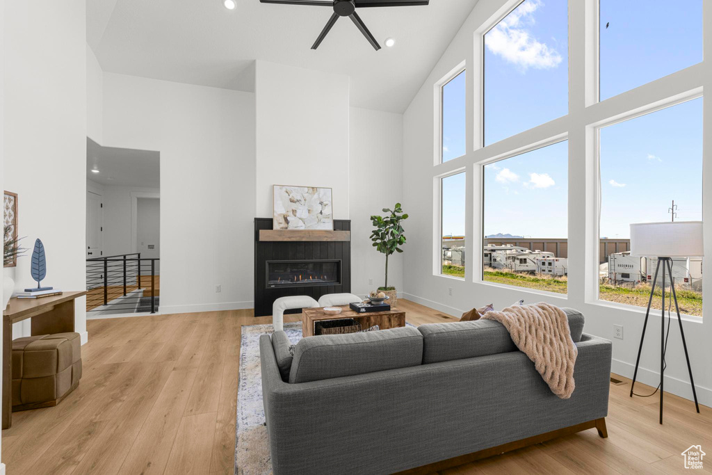 Living area featuring a towering ceiling, ceiling fan, baseboards, light wood finished floors, and a glass covered fireplace