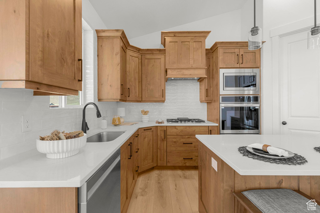 Kitchen with appliances with stainless steel finishes, a sink, light countertops, light wood finished floors, and decorative backsplash