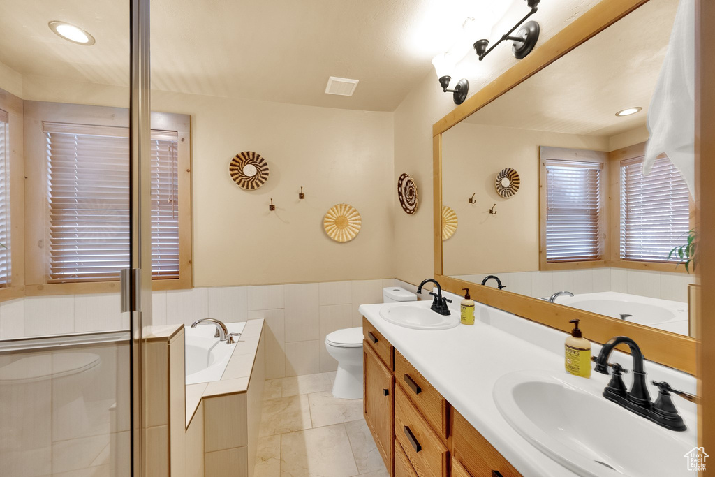 Full bathroom featuring toilet, a garden tub, double vanity, recessed lighting, and a wainscoted wall