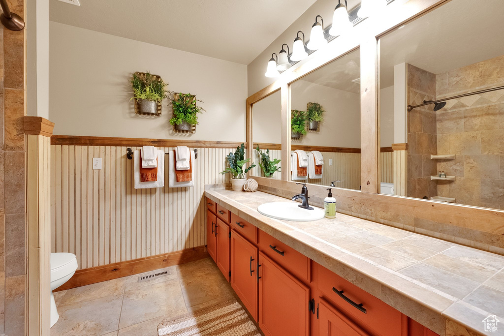 Bathroom with toilet, vanity, a shower, and a wainscoted wall
