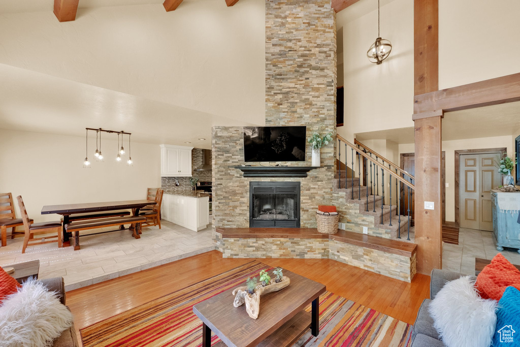 Living area with high vaulted ceiling, a stone fireplace, beamed ceiling, stairway, and light wood-style flooring