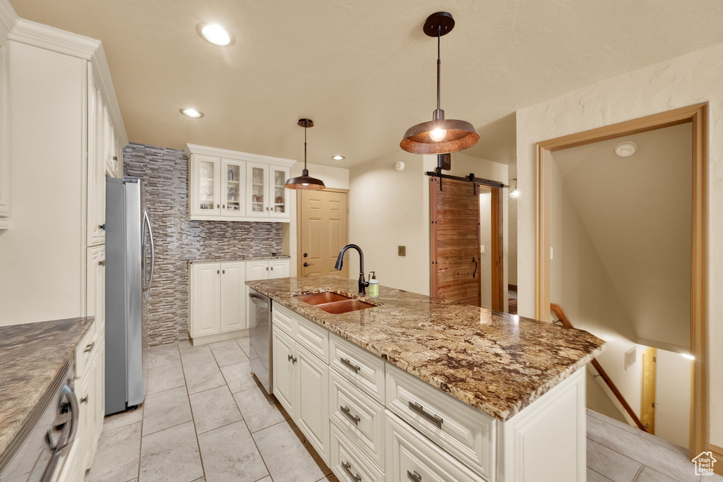 Kitchen with a barn door, appliances with stainless steel finishes, a sink, white cabinets, and recessed lighting
