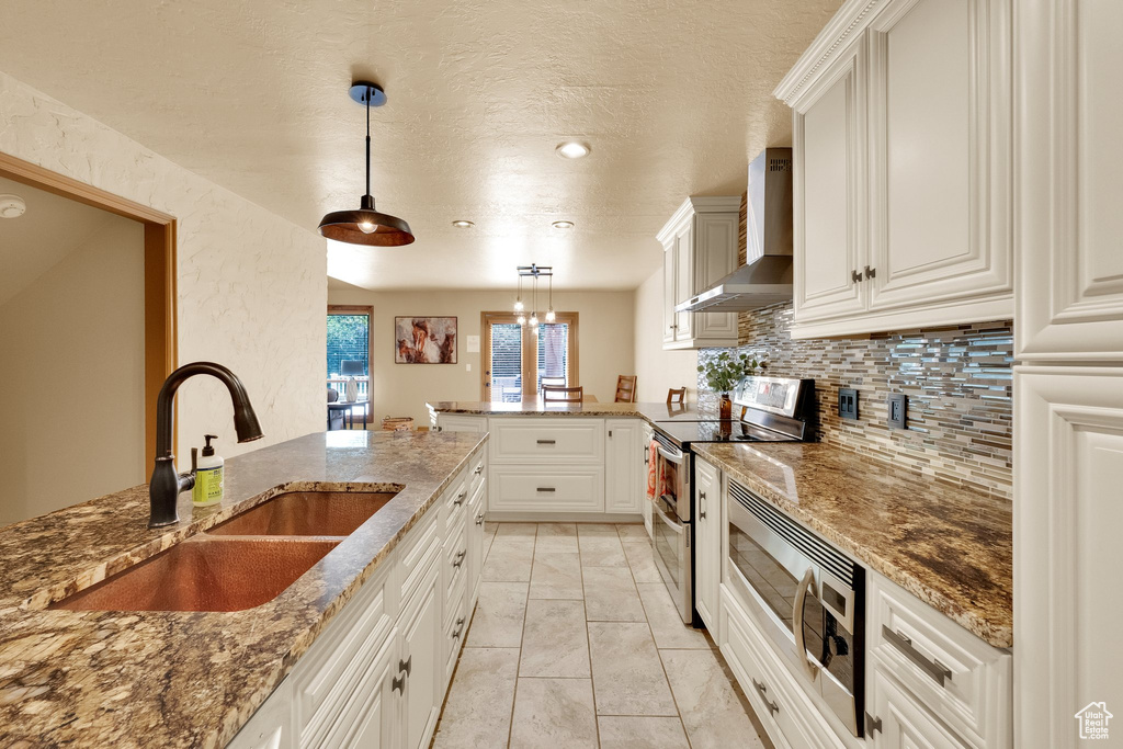 Kitchen with wall chimney range hood, appliances with stainless steel finishes, a sink, a peninsula, and tasteful backsplash