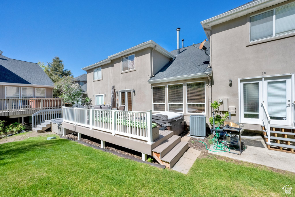 Back of house featuring stucco siding, a wooden deck, a lawn, central AC unit, and roof with shingles