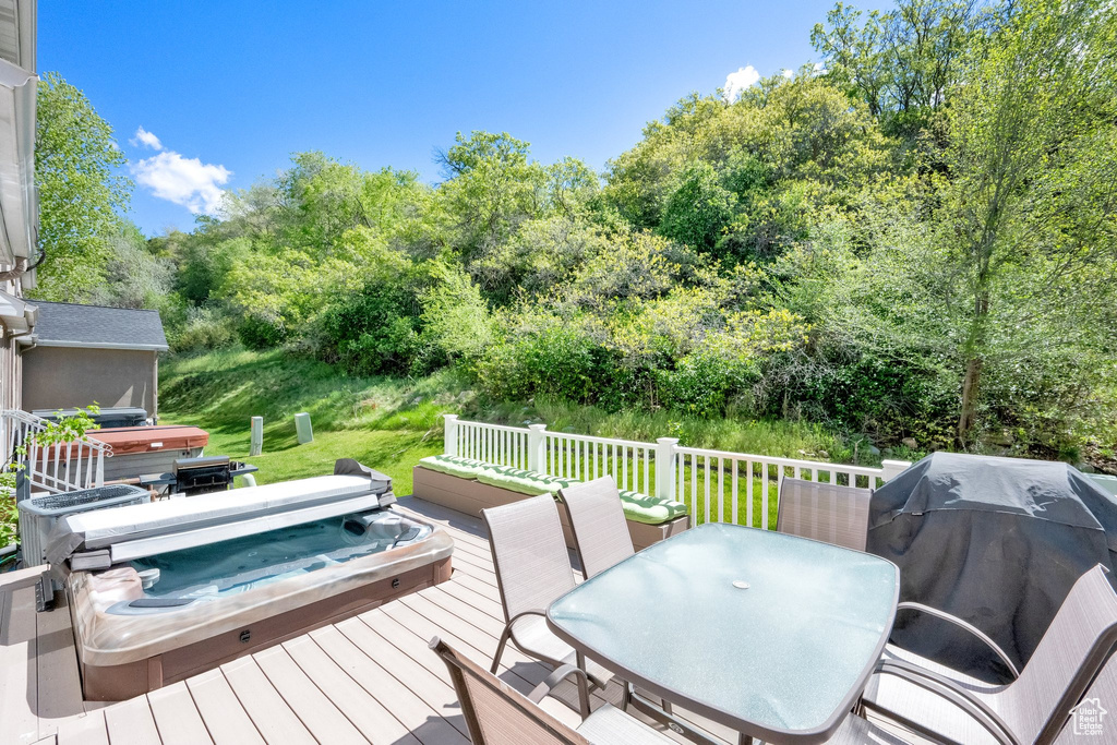 Wooden deck with a covered hot tub, area for grilling, outdoor dining space, and view of wooded area