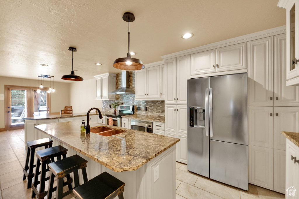 Kitchen with stainless steel appliances, wall chimney range hood, a sink, light tile patterned floors, and decorative backsplash
