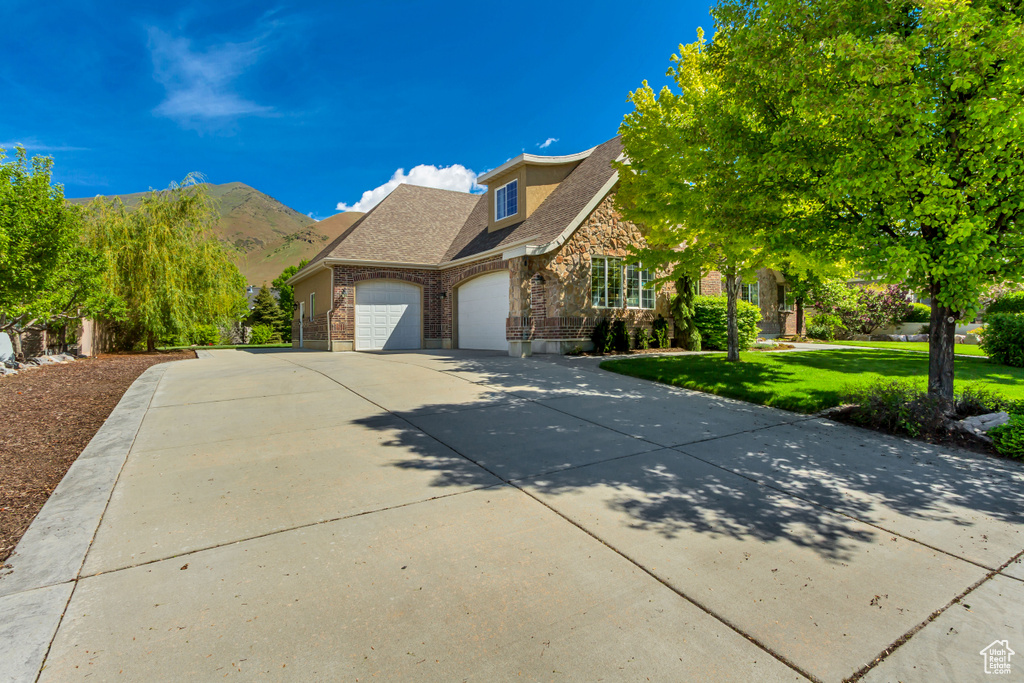 Traditional-style home featuring a garage, stone siding, a front yard, driveway, and brick siding