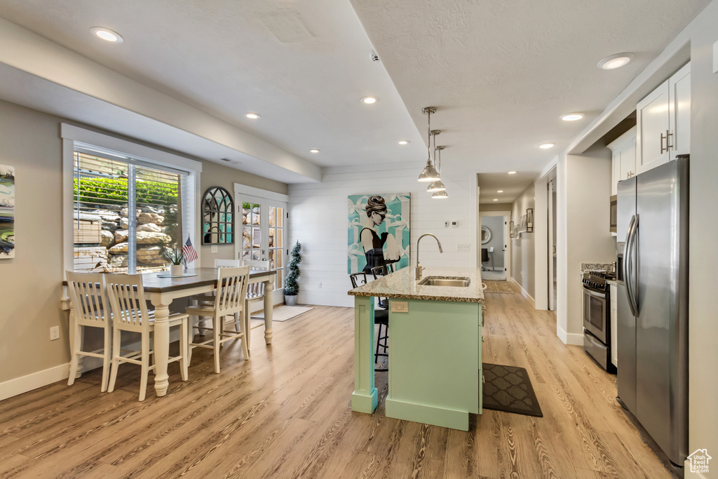 Kitchen with stainless steel appliances, a sink, light wood finished floors, white cabinetry, and a kitchen breakfast bar