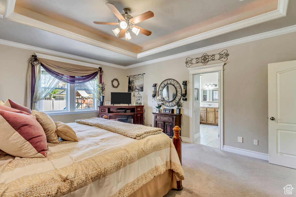 Bedroom with a raised ceiling, light colored carpet, ensuite bathroom, crown molding, and ceiling fan