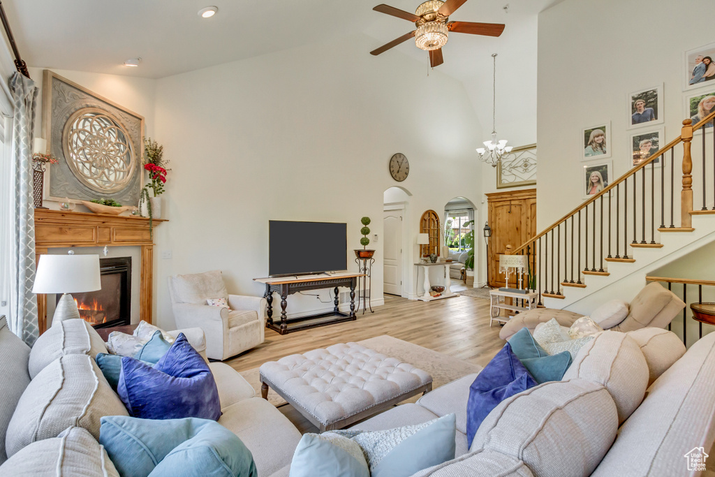 Living room with arched walkways, high vaulted ceiling, a glass covered fireplace, ceiling fan, and wood finished floors