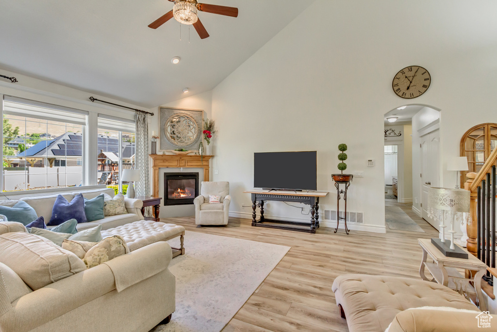 Living room with high vaulted ceiling, ceiling fan, arched walkways, a glass covered fireplace, and wood finished floors