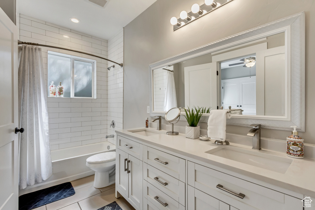 Full bathroom with shower / bath combo with shower curtain, double vanity, ceiling fan, toilet, and tile patterned floors
