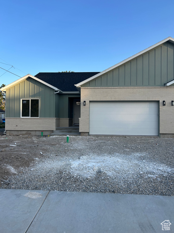 View of front of home with board and batten siding, a garage, brick siding, and gravel driveway