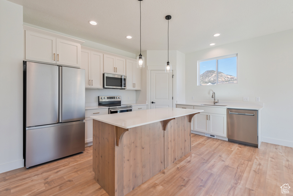 Kitchen with stainless steel appliances, a sink, light countertops, light wood-style flooring, and white cabinets
